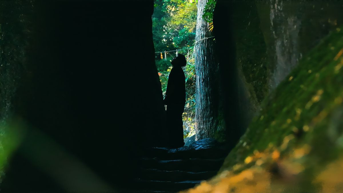 岩の隙間から神社の木立を見上げる人物のシルエット
