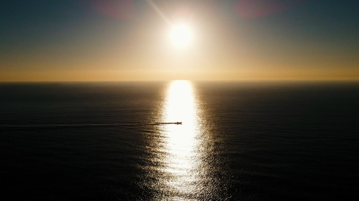 日の出を映す海原を走る一艘の船の空撮